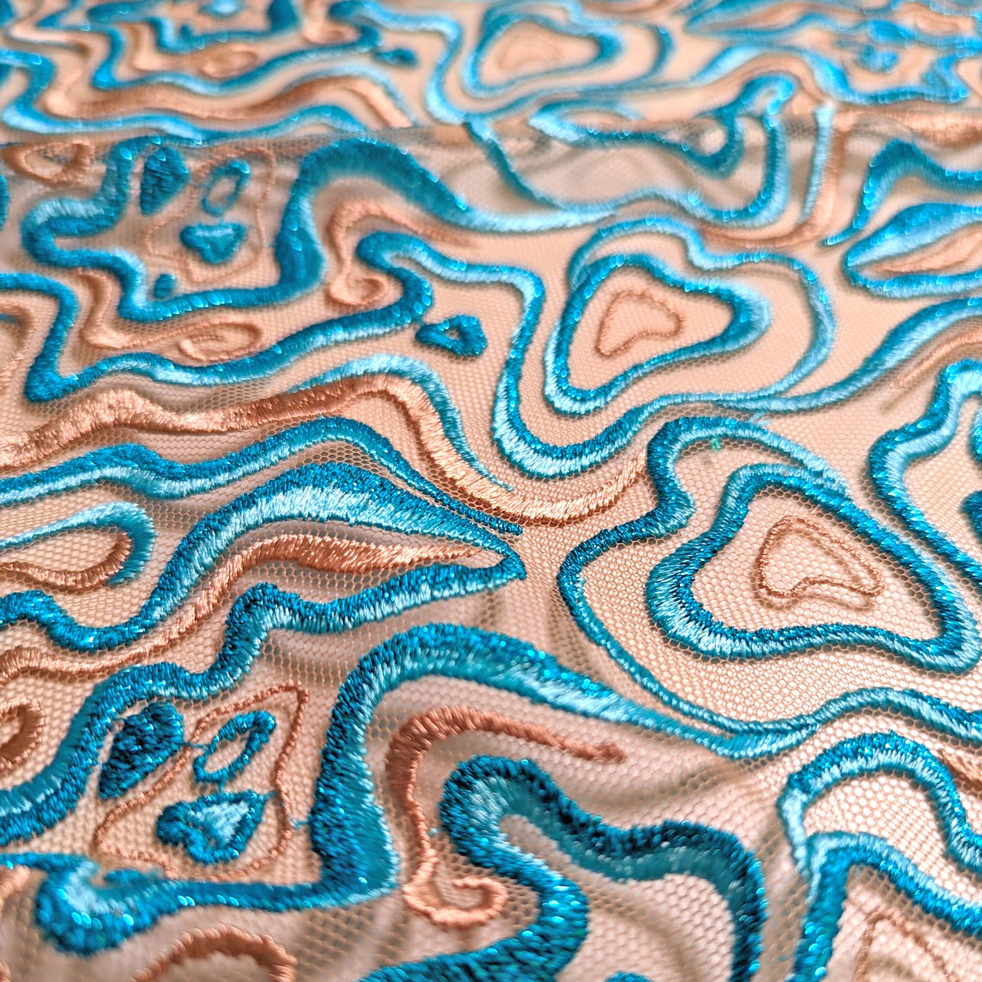 CLOSE UP OF BLUE AND TAUPE EMBROIDERY FEATURING GLITTERY YARNS ON SHEER TULLE BASE FABRIC