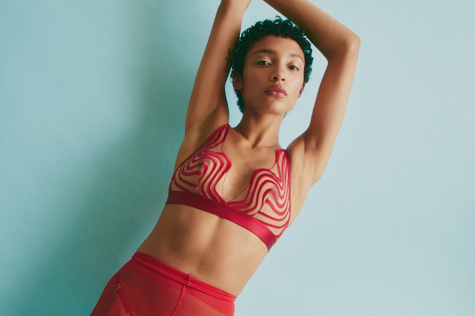 Woman in red fashion bra and  sheer red tights posing against a light blue background
